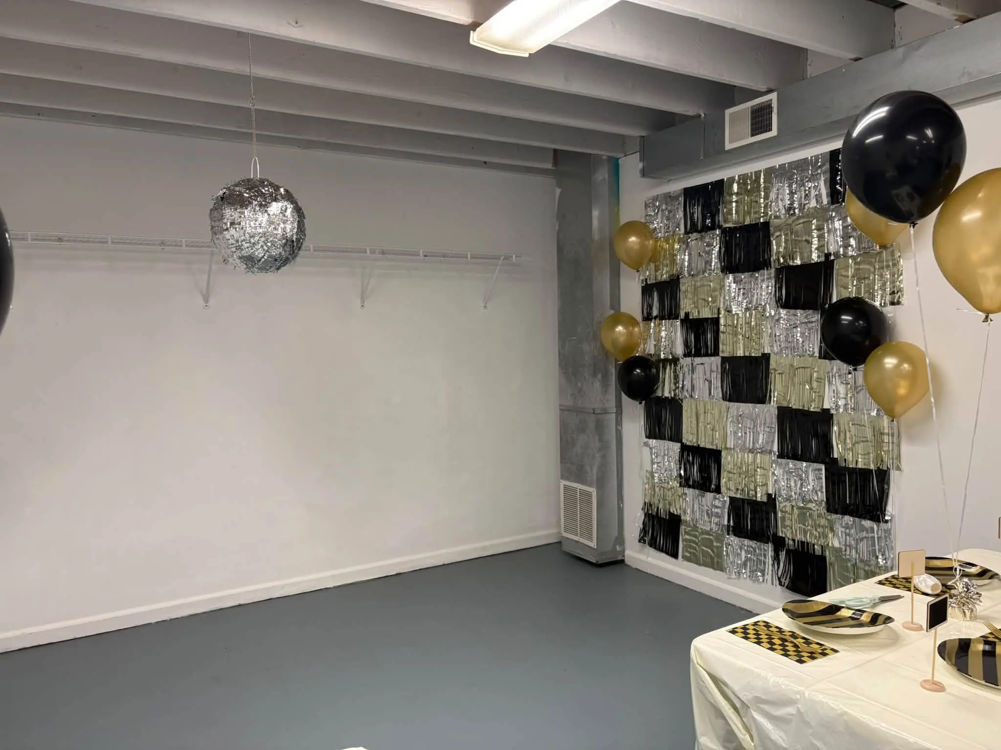 Room with a table covered in a white cloth and adorned with black and gold balloons