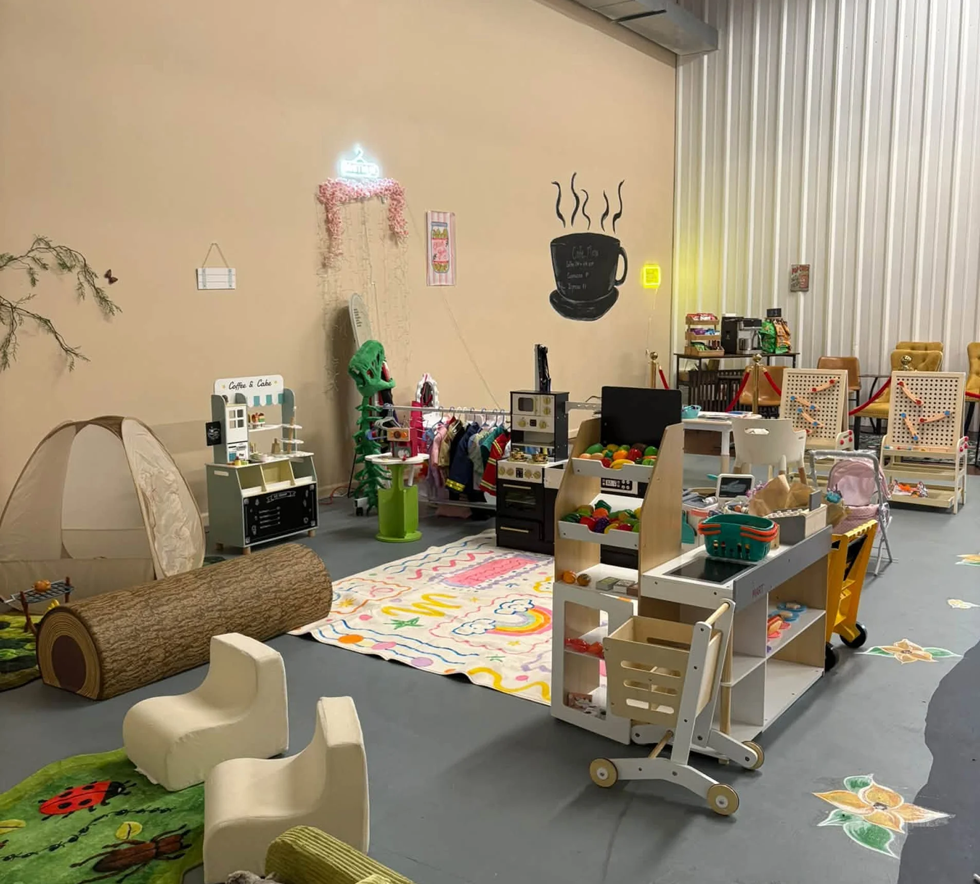 Room filled with lots of furniture and toys, including chairs, carpets on the floor, a tree trunk, a tent