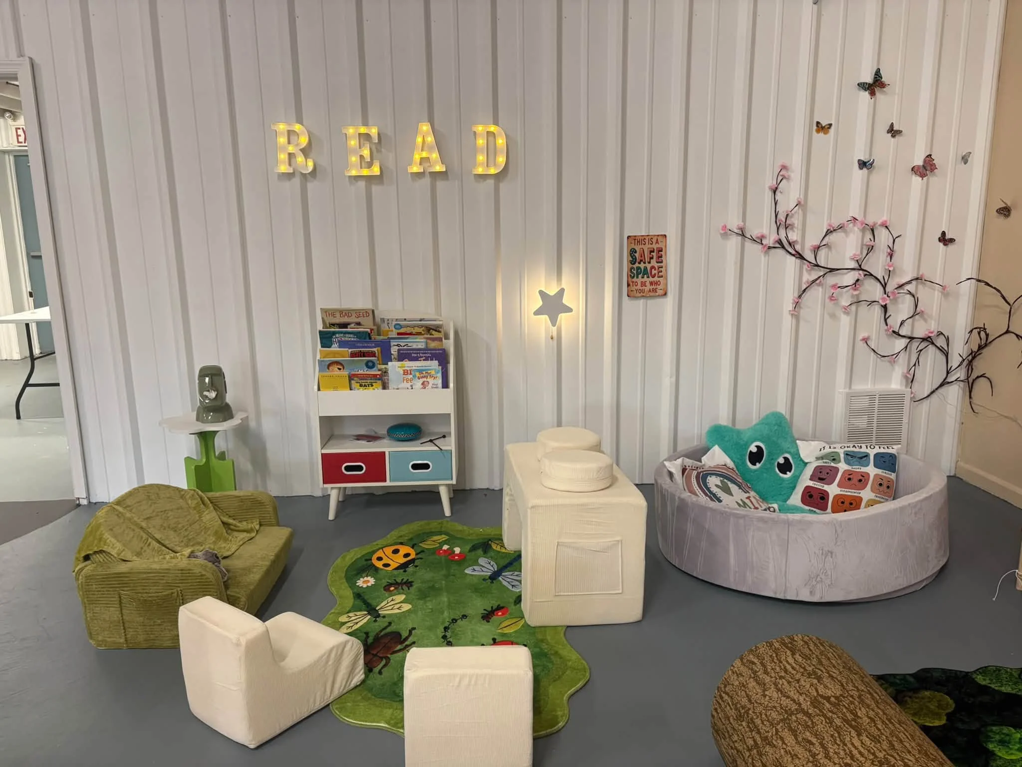 Room filled with lots of furniture, including sofas, pillows, a carpet on the floor, a cupboard with books